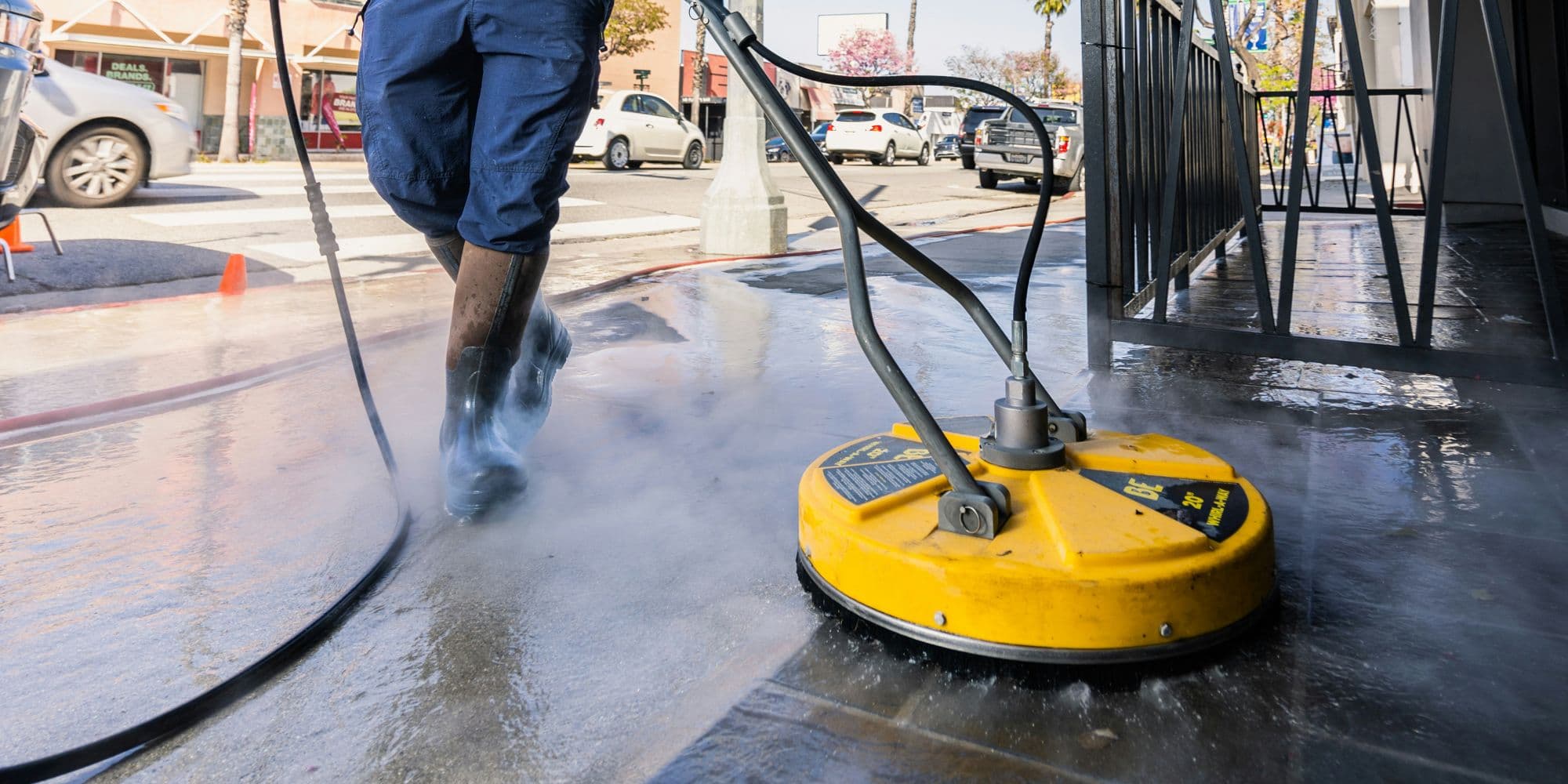 Surface cleaner attachment spraying and steaming as it pressure washes an outdoor paved walkway