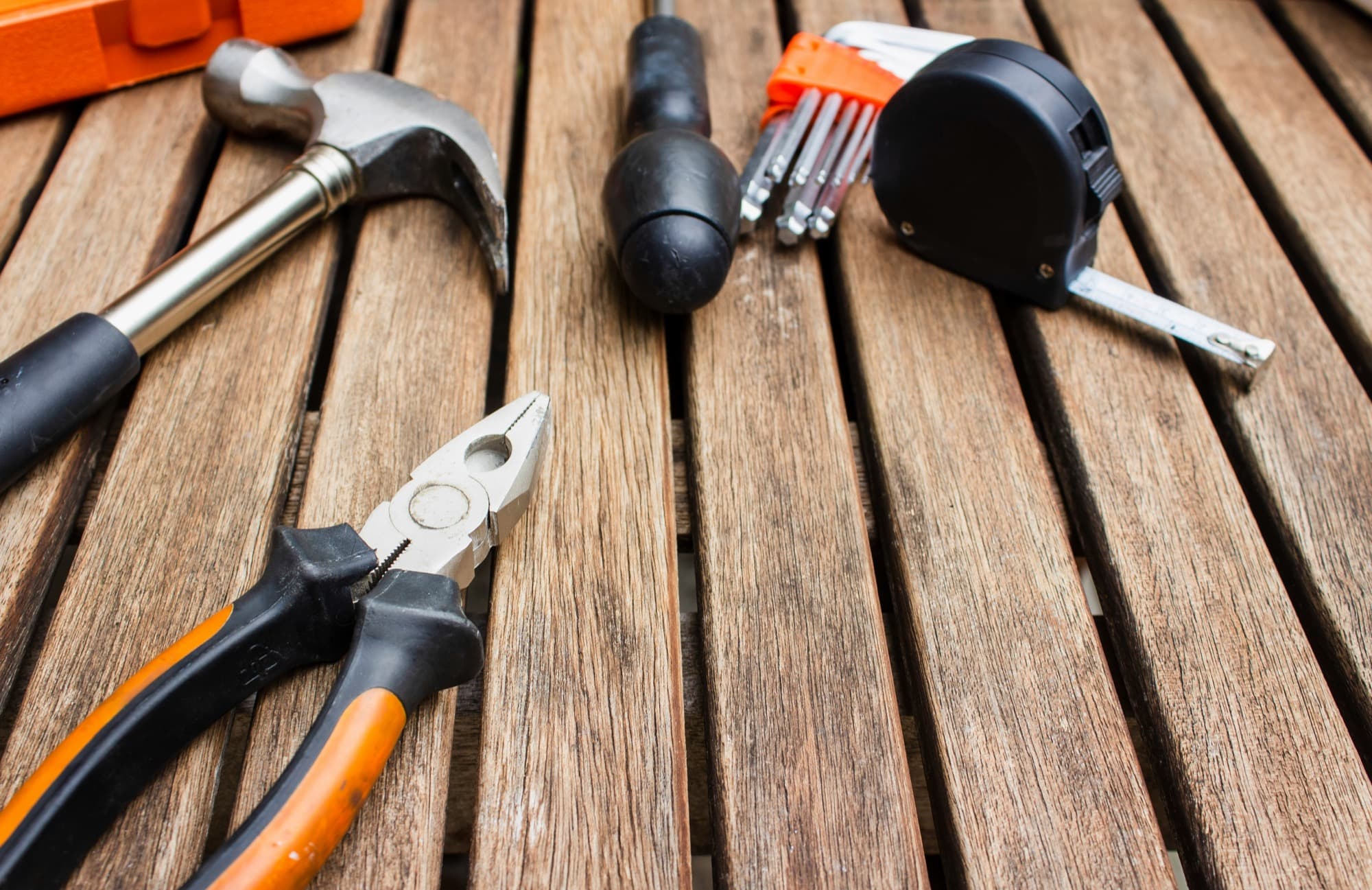 Hammer, pliers, hex keys and a tape measure laid out on weathered timber decking