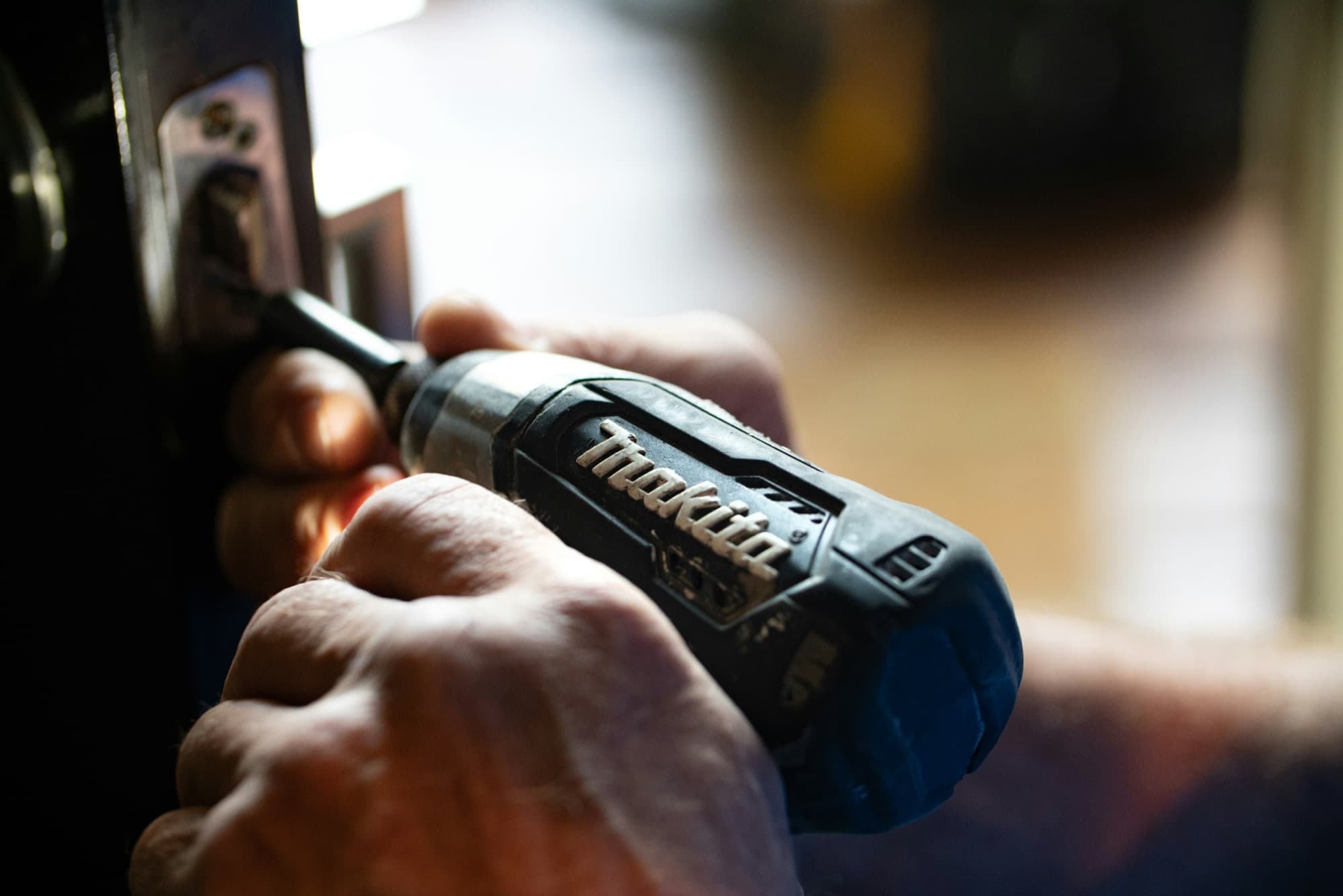 Close-up of hands using a cordless drill to adjust a door hinge