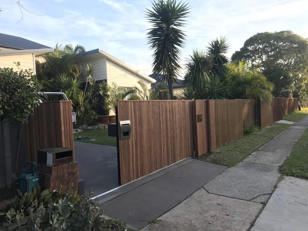 Timber slat fence and sliding driveway gate along a suburban street