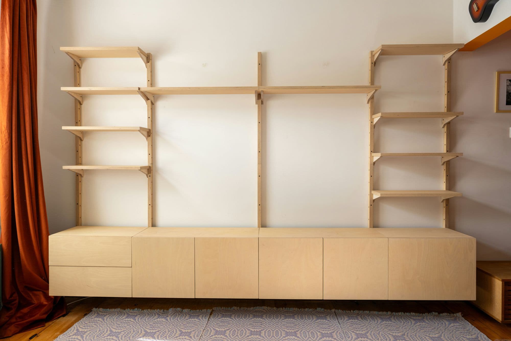 Built-in plywood shelving and cabinetry assembled and fitted along a living room wall