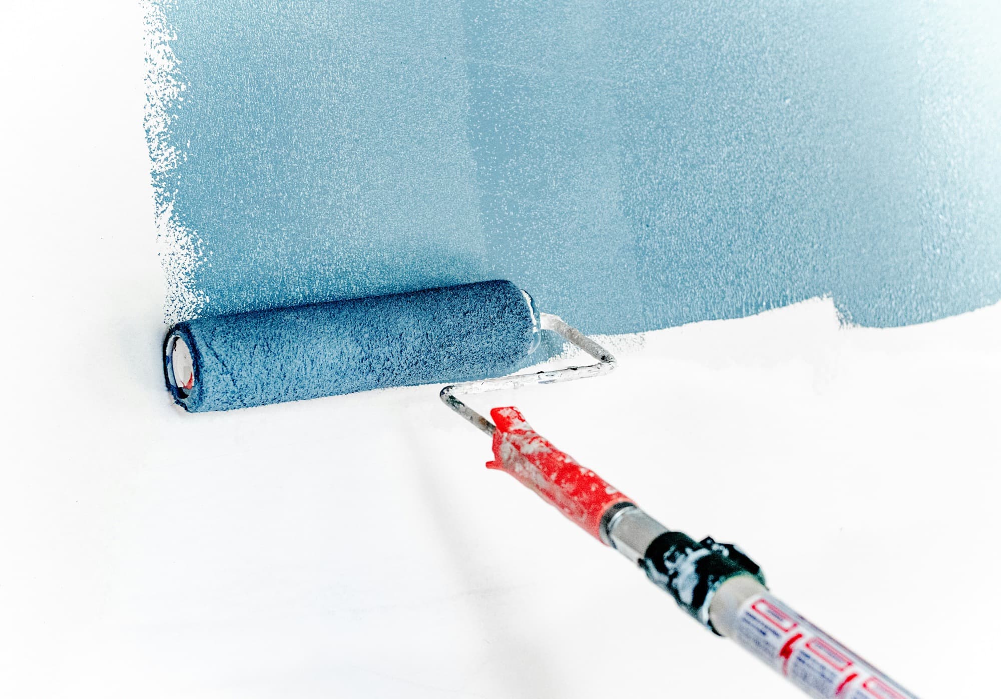 Paint roller applying blue paint to a white interior wall