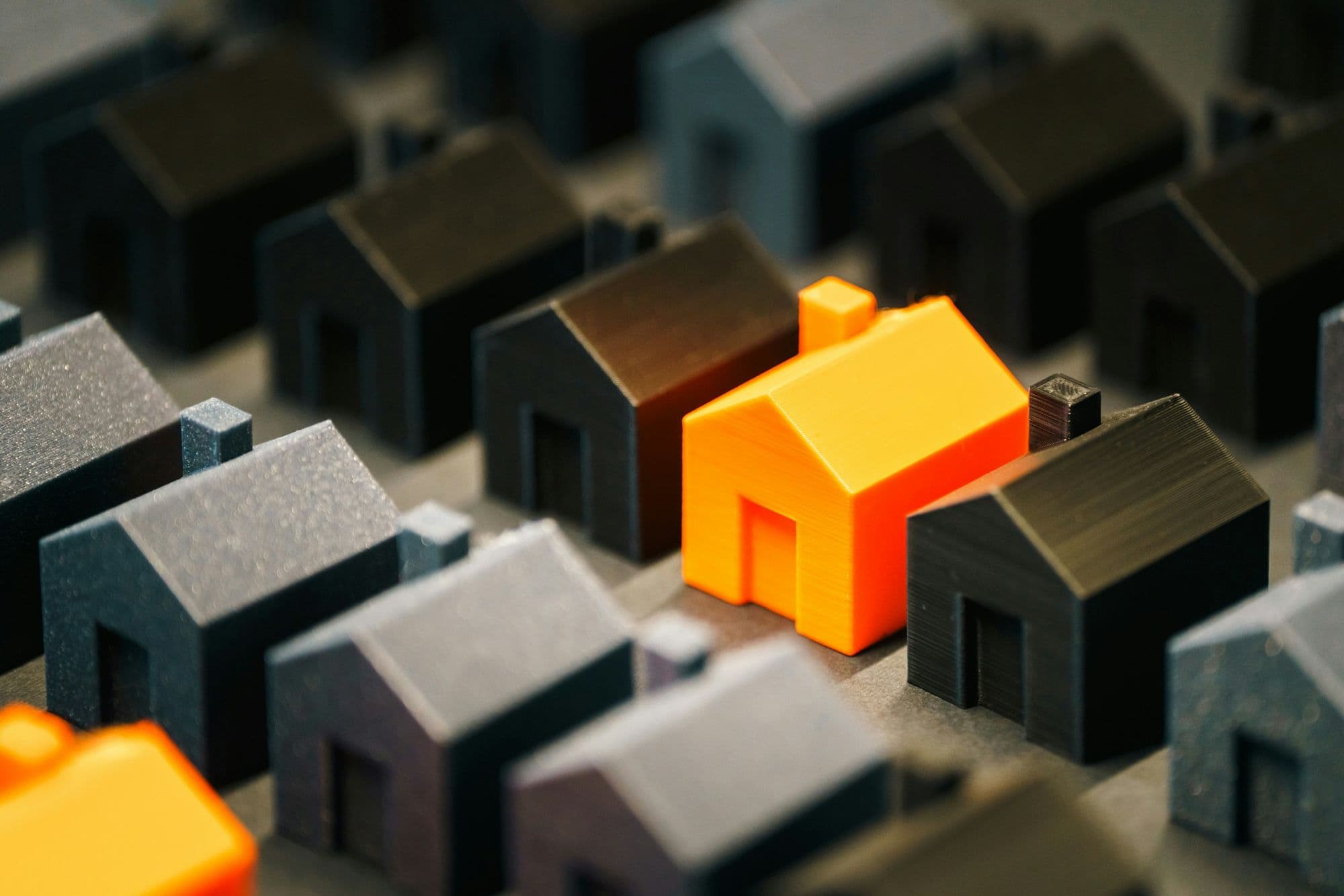 Rows of miniature model houses with one orange house standing out from the rest
